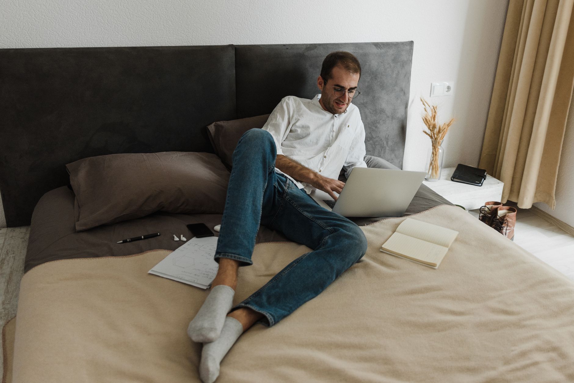 Hombre adulto trabajando en un portátil sentado en la cama en casa, en un ambiente informal y relajado.